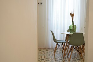Uma área de refeições com mesa e cadeiras, um vaso com flores secas e um chão estampado.