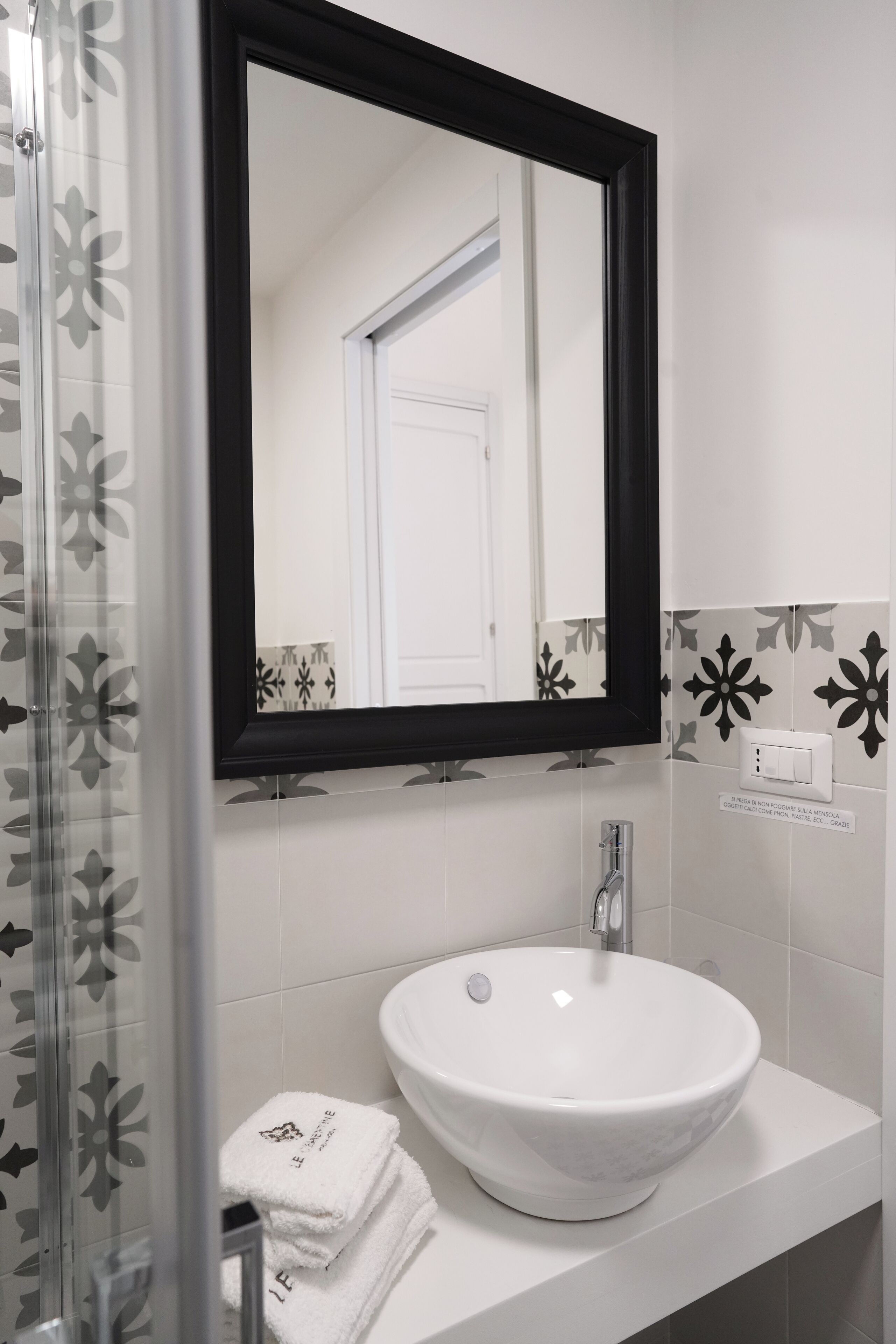 Une salle de bain avec un lavabo blanc, un miroir à cadre noir et une douche ornée d’un motif floral.