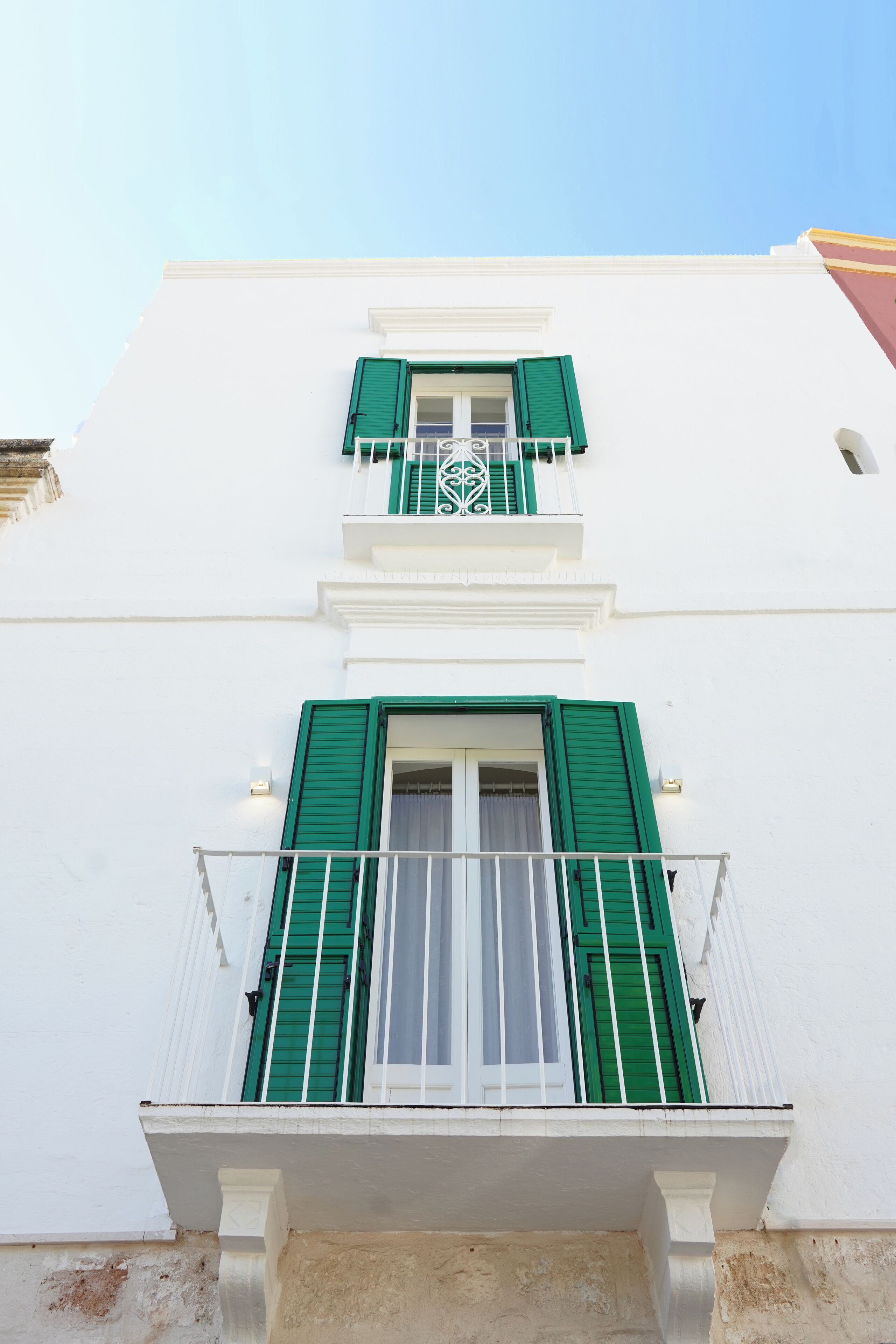 Ein Gebäude mit weißen Wänden und grünen Fensterläden, mit einem Balkon und einem weißen Geländer.