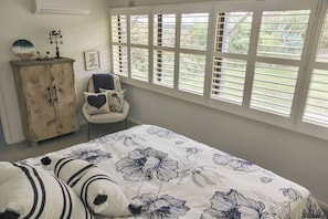 A bedroom with a large bed, a wooden cabinet, a chair, and a window with blinds. - .Beach getaway, pet friendly, coastal vibe (Aldinga Beach)