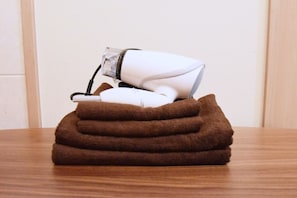 A white hair dryer on a brown towel on a wooden table.