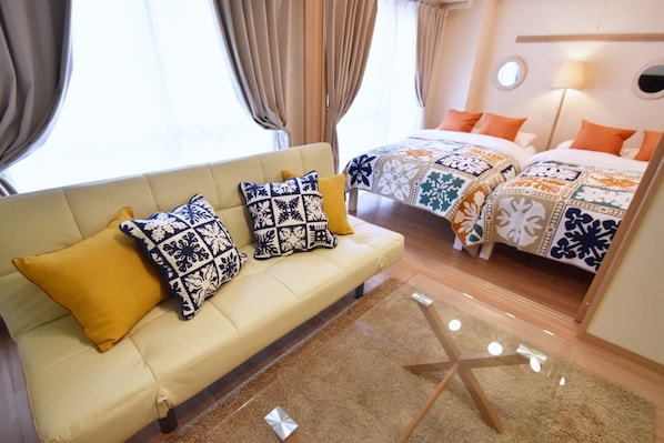 A hotel room with a sofa, two beds, a large window, curtains, and a lamp.