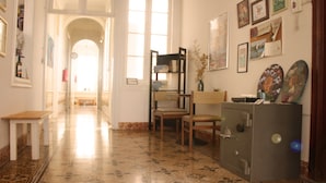 A hallway with a tiled floor, a wooden chair, a desk, a safe, and various framed pictures on the walls. - Mahalo Helthy House (Las Palmas de Gran Canaria)