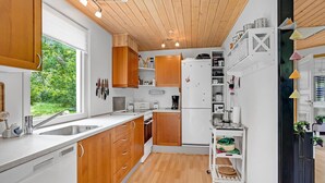 A modern kitchen with wooden cabinets, a white refrigerator, and a window providing a view of greenery outside. - Stunning home in Hadsund with WiFi (Hadsund)
