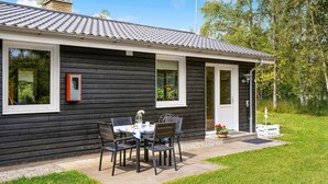 A small, dark wooden house with a tiled roof, a front door, and a patio with a table and chairs. - Stunning home in Hadsund with WiFi (Hadsund)