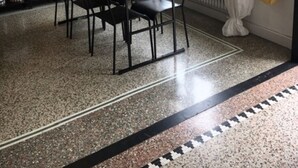Ein Essbereich mit Tisch und Stühlen, einem Blumentopf, einem Bücherregal und einem Fenster mit Vorhängen.