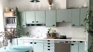 Eine moderne Küche mit türkisfarbenen Schränken, einer weißen Arbeitsplatte und einem Essbereich mit Tisch und Stühlen.