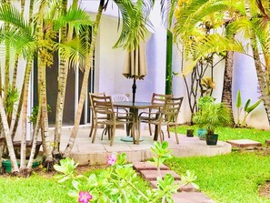 Relax in a serene garden setting with a patio featuring a round table and four chairs surrounded by lush tropical plants.