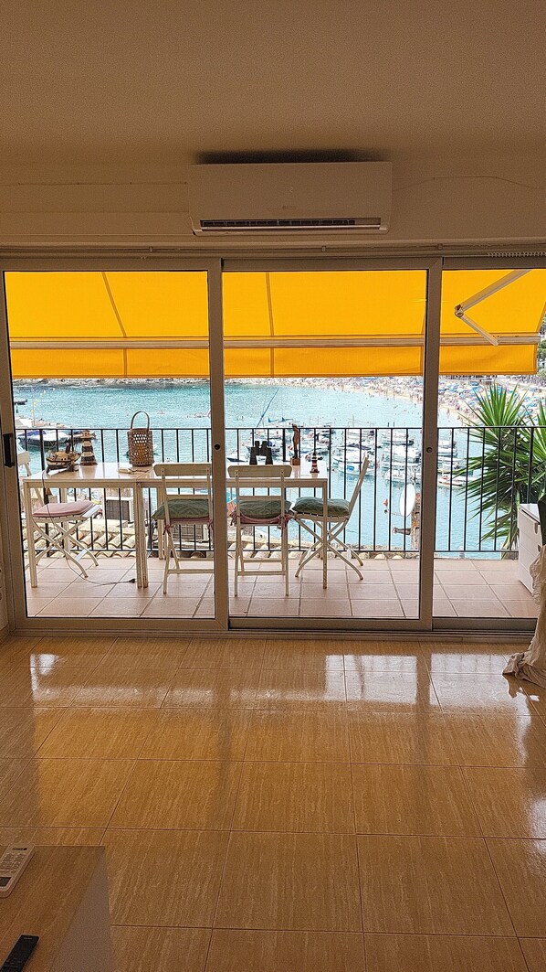 A room with a view of a marina, a table with chairs, and a window with yellow blinds. - Apartment across from the ocean (Llafranc)
