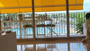 Un ampio balcone con tenda gialla, vista sulla spiaggia e una sedia bianca.