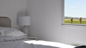 A bedroom with a bed, a bedside lamp, and a window with a view of a field. - Cosy Rural Lodge at Goldhill Glamping - Sleeps 4 (Shaftesbury)