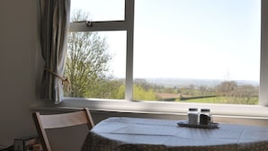 A room with a table set for two, a window with a view of a landscape, and a chair. - Cosy Rural Lodge at Goldhill Glamping - Sleeps 4 (Shaftesbury)