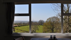 A room with a large window offering a view of a green field and trees. There is a sign above the window that reads "Cornfield Lodge." - Cosy Rural Lodge at Goldhill Glamping - Sleeps 4 (Shaftesbury)