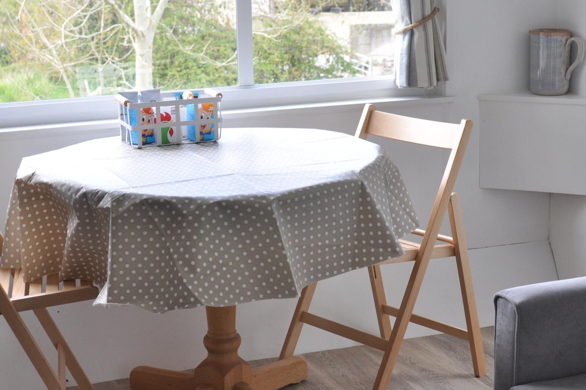A round table with a polka dot tablecloth, a wooden chair, and a small table with colorful items on it.