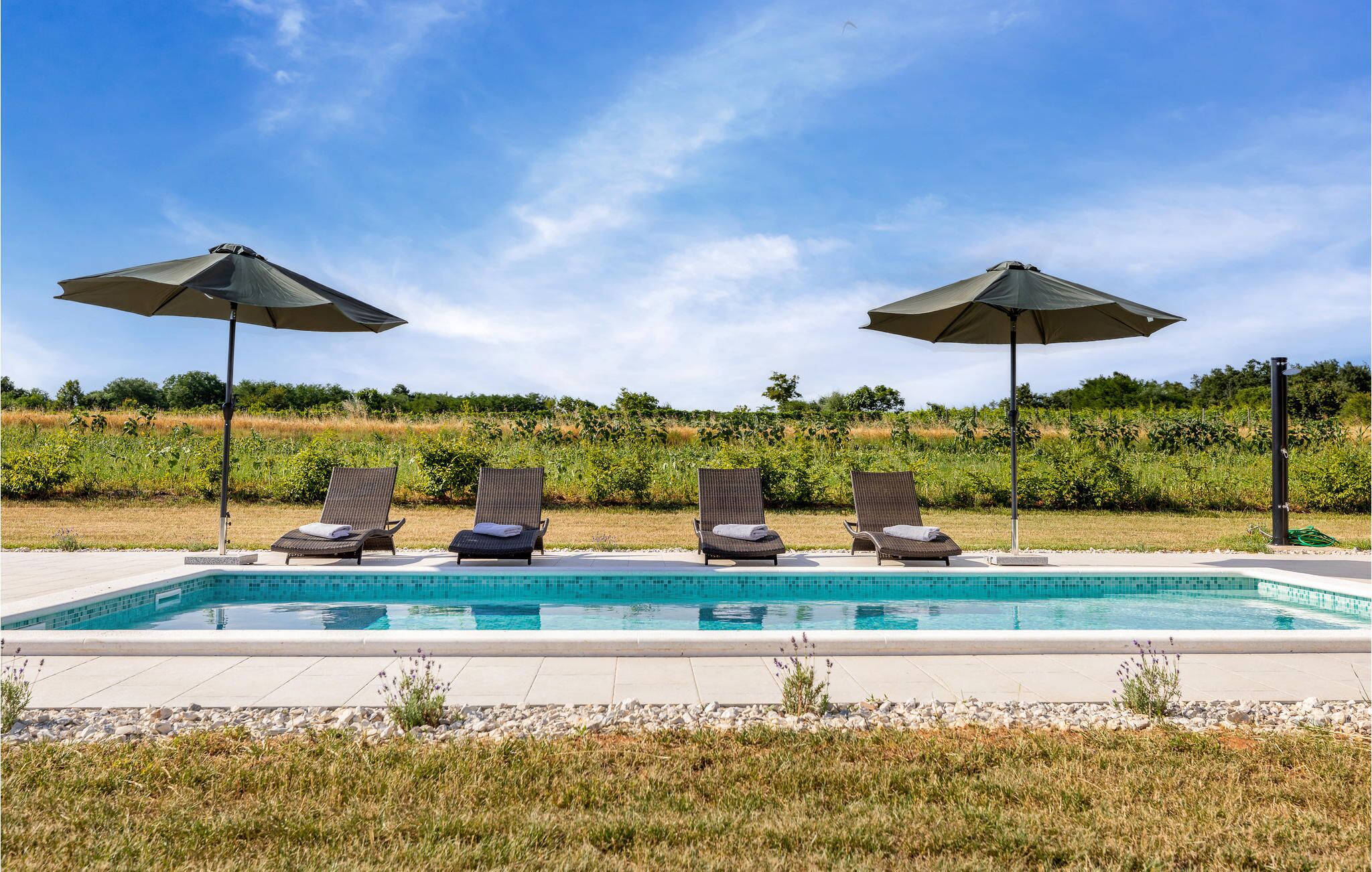 A pool with four sun loungers and two umbrellas.