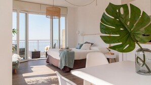 Une chambre moderne avec une grande fenêtre, un lit doté d’une tête de lit blanche, une table de chevet et une grande plante verte.