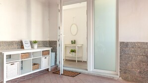 Un couloir avec une console blanche, des paniers en osier, un panneau d’accueil et une porte-fenêtre coulissante donnant sur une pièce décorée d’un miroir et de cactus.