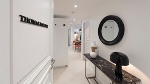 Un couloir moderne, avec une enseigne portant l’inscription « THOMAS MOORE » sur le côté gauche, un miroir rond sur le côté droit et une console en marbre surmontée d’une lampe.