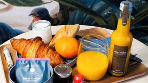 Bandeja de desayuno con cruasanes, jugo de naranja, vaso de leche, botella de jugo de naranja y una bolsita de té.