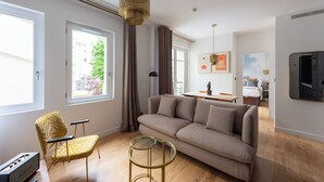 En moderne stue med en sofa, et sofabord i glas, en lænestol og en hængende lampe.