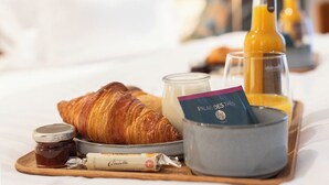 En bakke med morgenmad, inklusive croissant, marmelade, honning, et glas appelsinjuice og et lys med teksten "Palais des Thés".