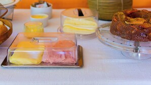 A breakfast buffet with various food items, a vase with flowers, and a wooden cabinet in the background. - VOA Pousada Recanto dos Colibris (Paraty)