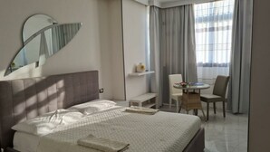 A hotel room with a large bed, a desk, a chair, a mirror, and a window with curtains.