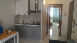 A modern kitchen with grey cabinets, stainless steel appliances, and a wooden table with a blue bottle and a glass.