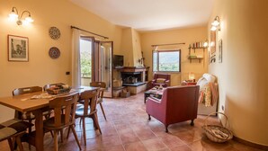 Un salon chaleureux avec une cheminée, un coin repas avec des meubles en bois et une vue sur l’extérieur par une fenêtre.