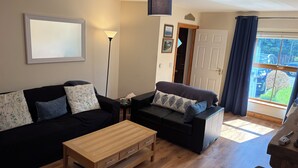 A living room with a sofa, a coffee table, a lamp, and a view through a window. - Townhome Manorhamilton (Manorhamilton)