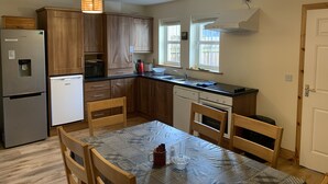 A compact kitchen with wooden cabinets, a refrigerator, a dishwasher, a sink, and a dining table with chairs. - Townhome Manorhamilton (Manorhamilton)