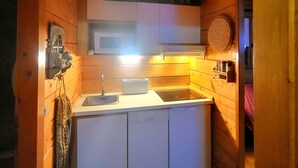 A compact kitchen with wooden walls, a white countertop, a microwave, a toaster, and a sink.