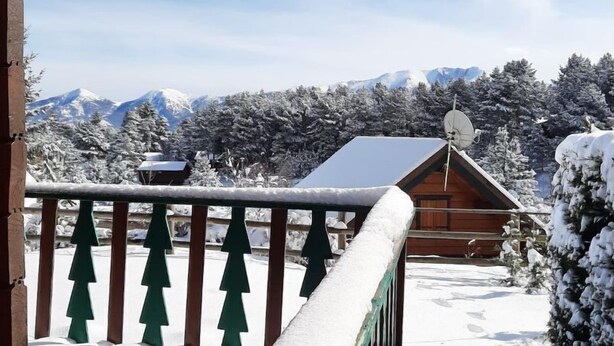 A wooden cabin with a snow-covered balcony overlooking a snowy mountain landscape.
