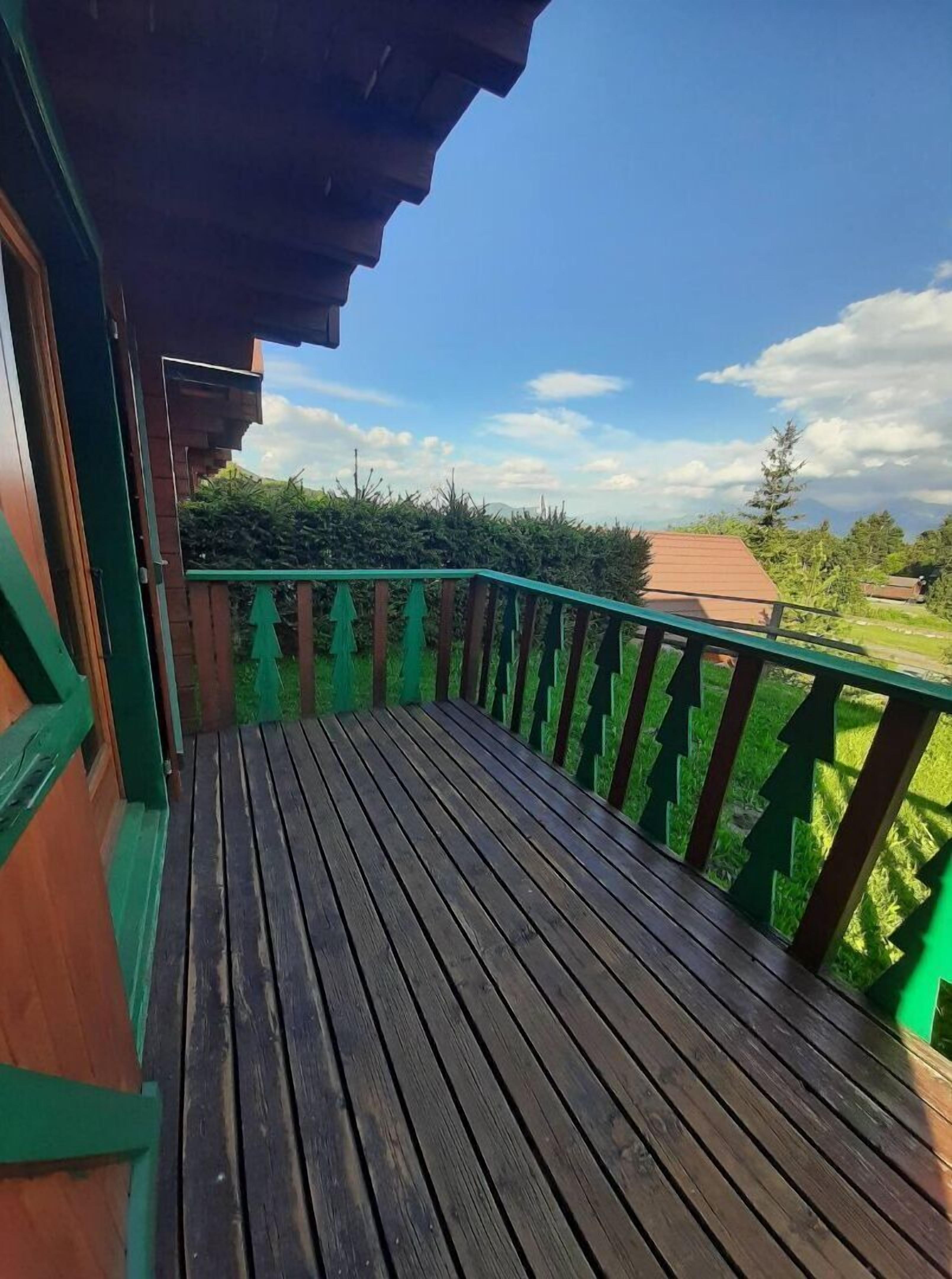 A wooden deck with a green railing, leading to a building with a brown roof.