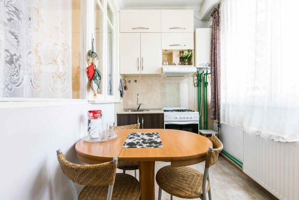 A compact kitchen with white cabinets, a gas stove, and a dining area with a wooden table and wicker chairs.
