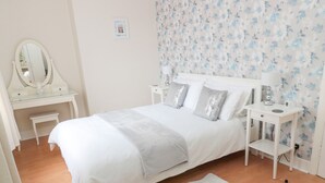 A bedroom with a bed, a white desk, a mirror, and a nightstand with a lamp. - Sandy Toes Cottage (Newbiggin-by-the-Sea)