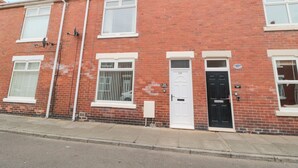 A row of red brick terraced houses with white-framed windows and doors, numbered 29 and 27. - Sandy Toes Cottage (Newbiggin-by-the-Sea)