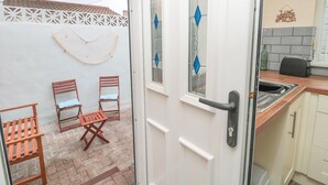 A kitchen with a sink, a toaster, and a window with blue diamond-shaped glass. There are two wooden chairs and a small table outside the door. - Sandy Toes Cottage (Newbiggin-by-the-Sea)