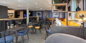 A modern cafe with tables and chairs, a bar area, and a seating area with a sofa and lamp. - ACE Hôtel Lyon Vénissieux (Venissieux)