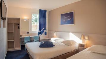 A hotel room with a bed, desk, chair, wardrobe, and a window with curtains.