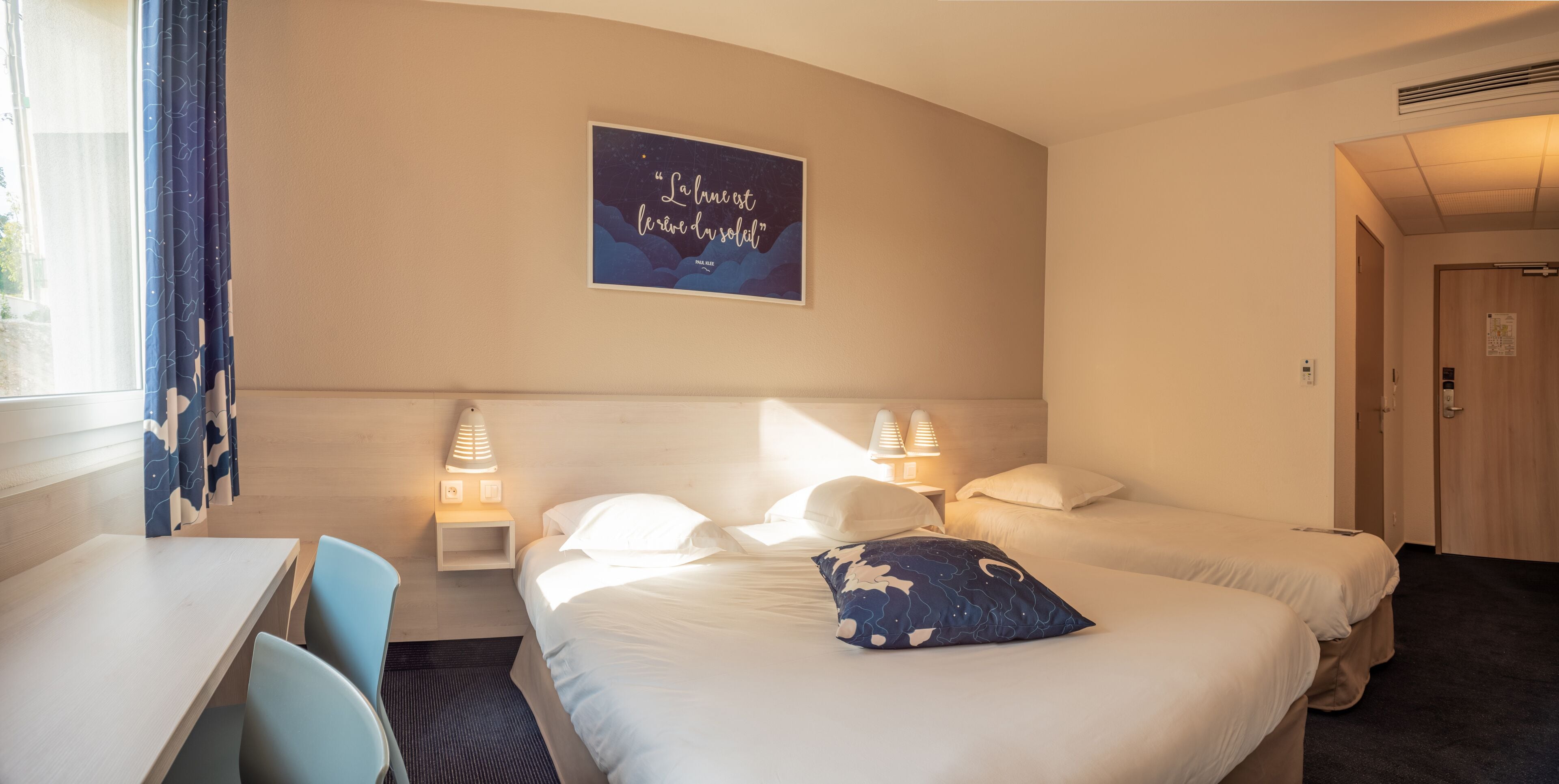 Habitación de hotel con dos camas, un escritorio y una silla. Hay un cartel en la pared y dos lámparas de noche.