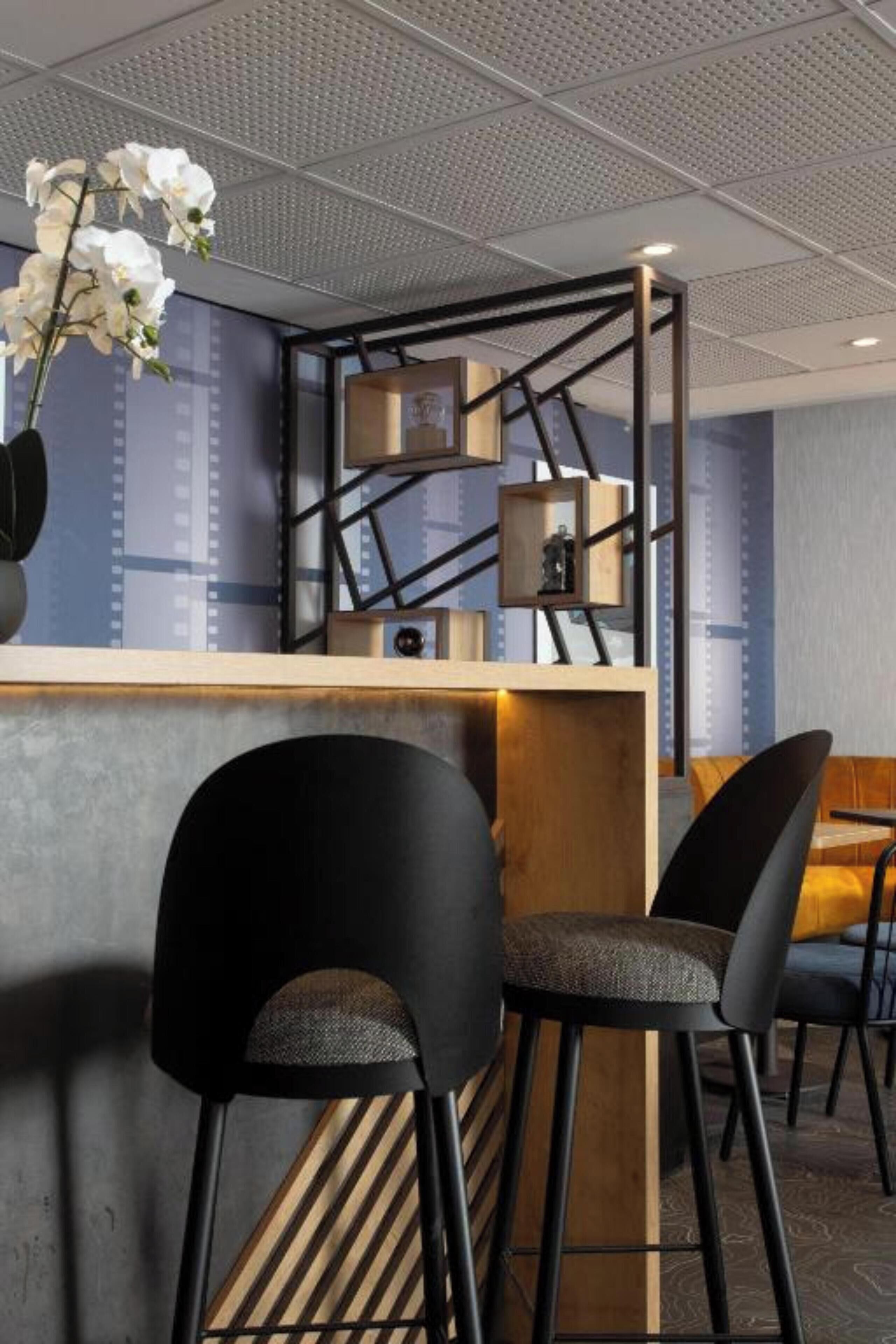 A modern bar area with a wooden counter, black chairs, and a decorative orchid arrangement.