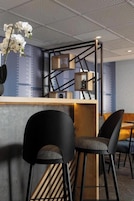 Zona de bar moderna con mostrador de madera, sillas negras y una decoración de orquídeas.