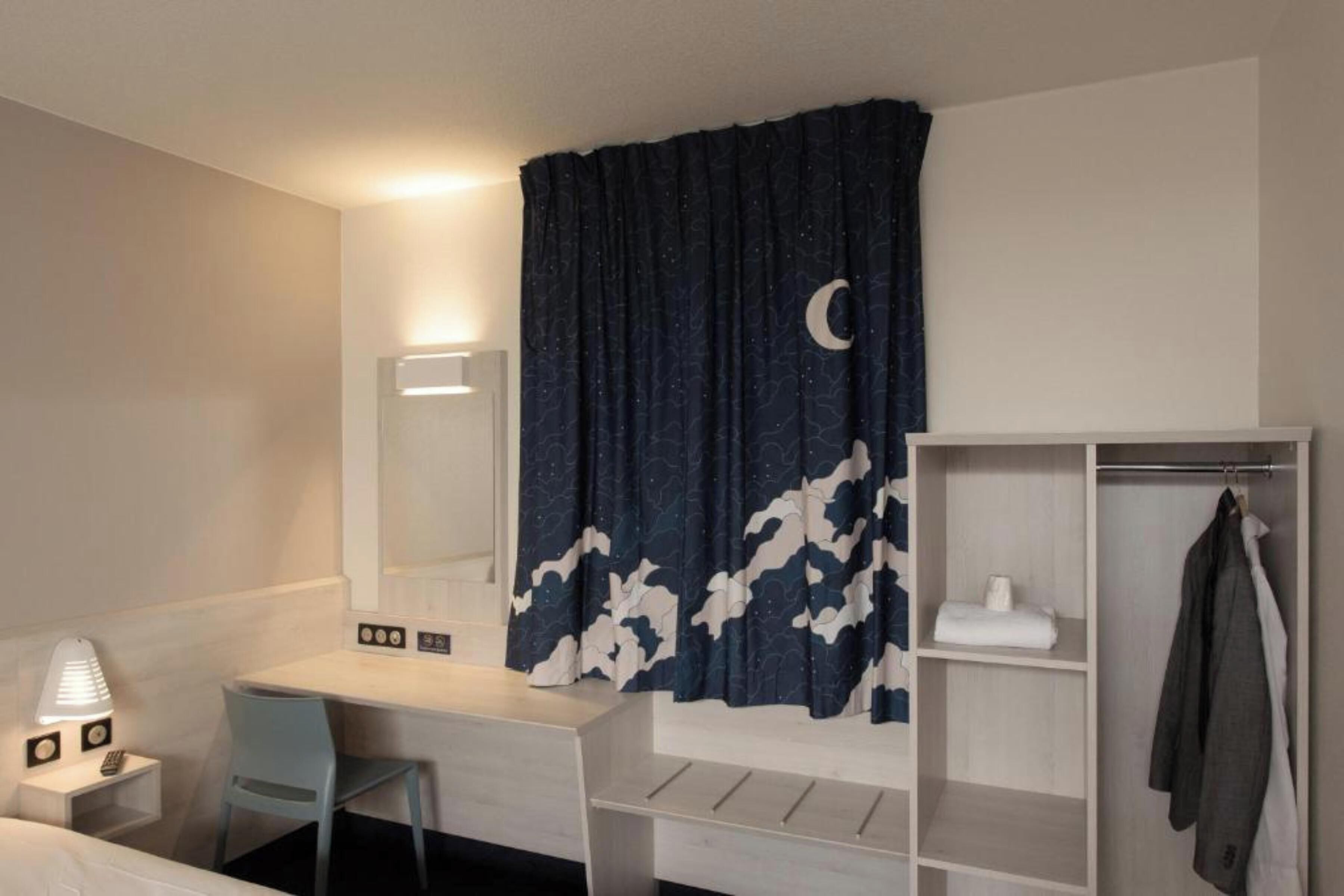 A hotel room with a desk, chair, and a wardrobe.