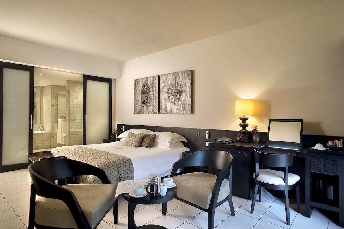 Una habitación de hotel moderna con cama, escritorio, sillas y zona de ducha.
