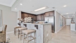 A modern kitchen with a central island, bar stools, wooden cabinets, stainless steel appliances, and a decorative fish sculpture. - New Complex!  Lazy River/Slide, 2BR Beachfront! (Orange Beach)