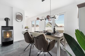 Eine moderne Küche mit Kaminofen, einem Essbereich mit Tisch und Stühlen sowie Blick auf Häuser durch große Fenster.