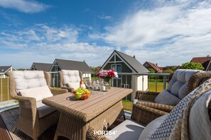 A balcony with wicker furniture, a table with a fruit bowl and flowers, and a view of houses.