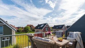 Une terrasse dotée de meubles en osier, d’une table sur laquelle est posé un panier de fruits, et d’où l’on peut admirer les maisons voisines.