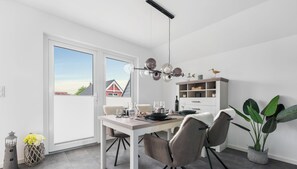 Un comedor moderno con una mesa preparada para cuatro personas, una araña y vistas al exterior a través de una puerta corredera.